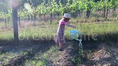 小女孩穿花裙和白帽子。 小女孩给花园浇水